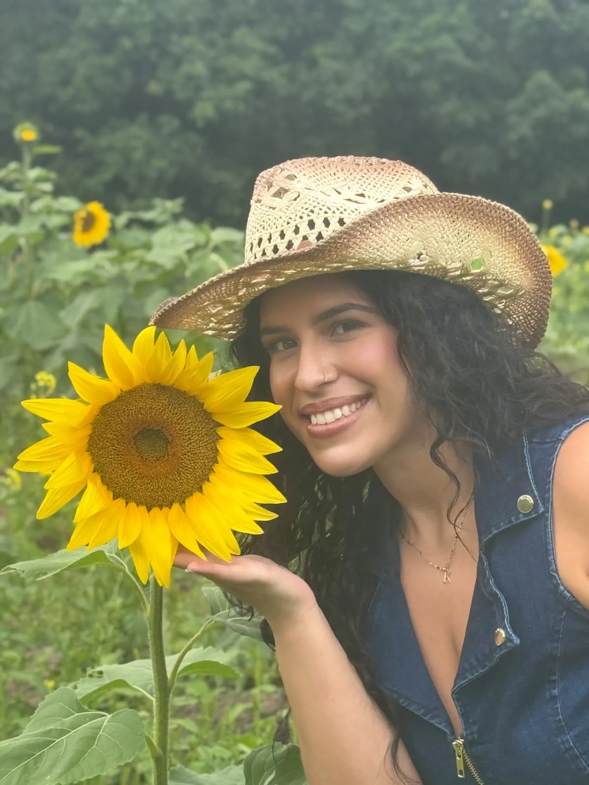 Katherinne, licensed esthetician and owner of Glow Fusion Esthetic in Armonk, NY, wearing a straw hat and holding a sunflower in a sunflower field